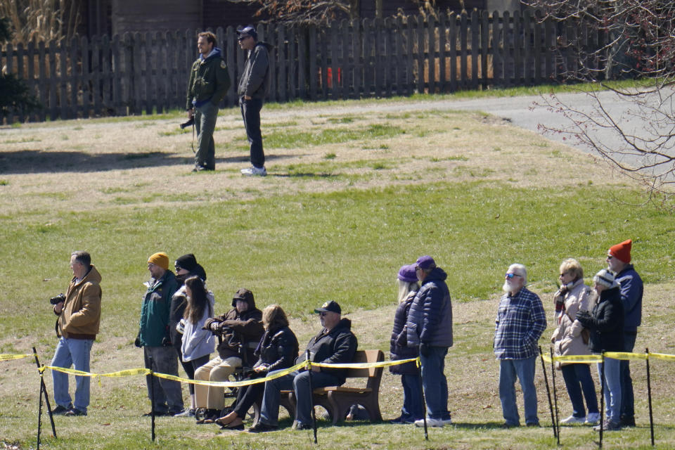 People sit on a park as they watch crews work to refloat the container ship Ever Forward, which ran aground in the Chesapeake Bay, Tuesday, March 29, 2022, in Pasadena, Md. (AP Photo/Julio Cortez)