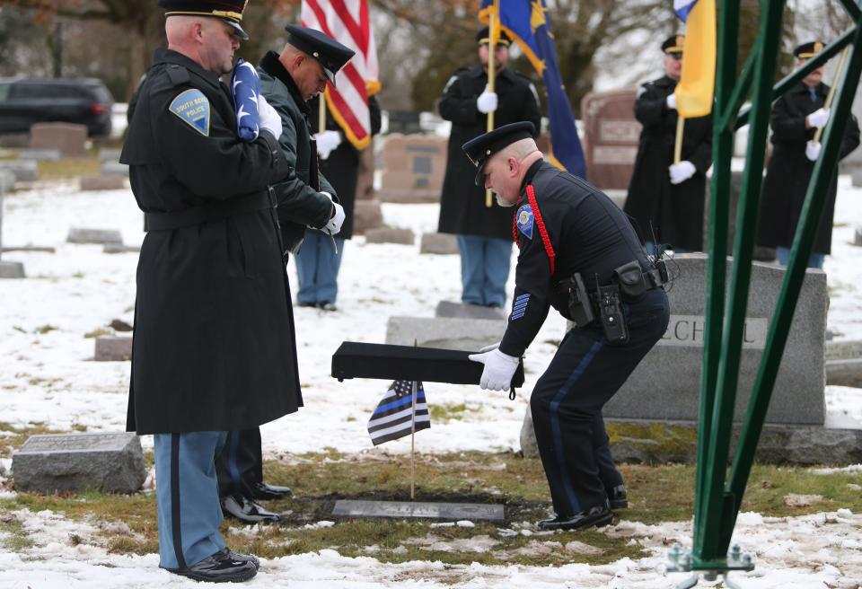 South Bend Police Patrolman and Chaplain James Burns uncovers a grave marker Wednesday, Jan. 10, 2024, at the grave marker dedication service for South Bend Police Officer Fred E. Buhland, who died in the line of duty 103 years ago — on Jan. 10, 1921 — and had been buried in an unmarked grave in Highland Cemetery.