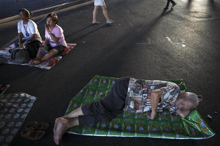 An anti-government protester sleeps on a road as others listen to a speech at the main intersection which protesters are occupying in downtown Bangkok February11, 2014. REUTERS/Damir Sagolj