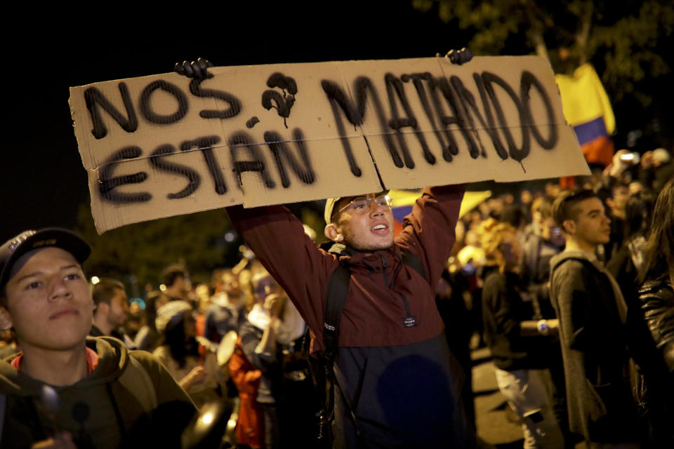 An anti-government protester holds a sign with a message that reads in Spanish: "We are being killed," in Bogota, Colombia, Saturday, Nov. 23, 2019. Authorities in Colombia are maintaining a heightened police and military presence in the nation's capital following two days of unrest. (AP Photo/Ivan Valencia)