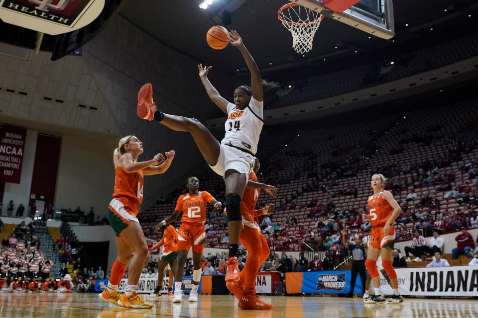 Oklahoma State's Taylen Collins (14) falls to the court after getting fouled by Miami's Lashae Dwyer (13) during the second half of a first-round college basketball game in the women's NCAA Tournament Saturday, March 18, 2023, in Bloomington, Ind. (AP Photo/Darron Cummings)