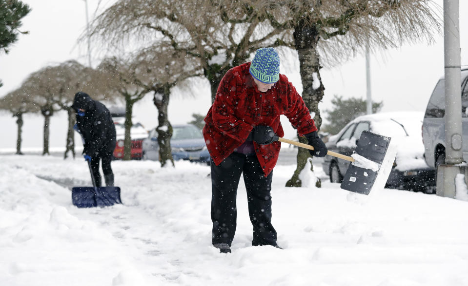 Condo owners Suzanne Wittmann, right, and Jennifer Stock clear the sidewalk in front of their building following several more inches of snow that fell overnight Monday, Feb. 11, 2019, in Seattle. Schools and universities closed across Washington state and the Legislature cancelled all hearings as the Northwest dealt with snow and ice and prepared for more as a series of winter storms socked the region. (AP Photo/Elaine Thompson)