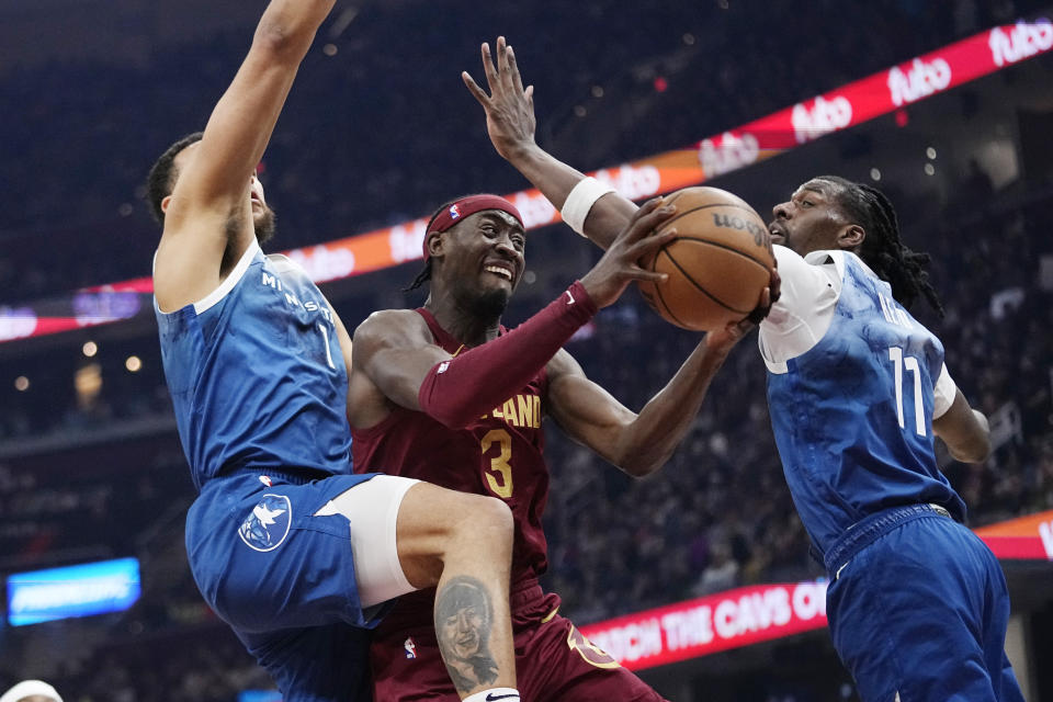 Minnesota Timberwolves forward Jaden McDaniels (3) drives between Minnesota Timberwolves forward Kyle Anderson (1) and center Naz Reid (11) during the first half of an NBA basketball game Friday, March 8, 2024, in Cleveland. (AP Photo/Sue Ogrocki)