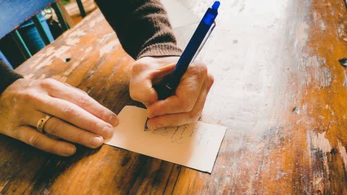 Close-up of female hand writing a grocery list on a vintage wooden table.