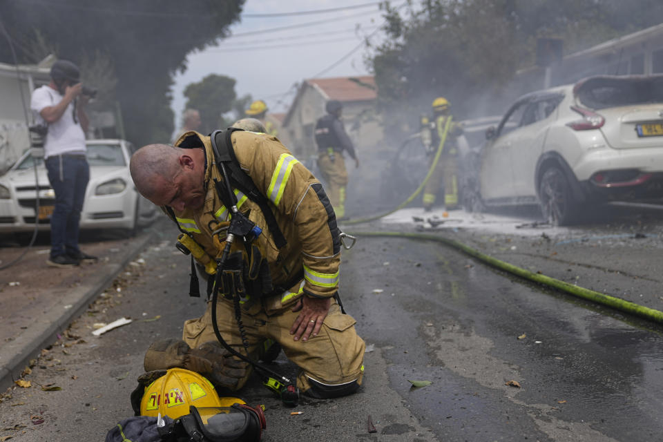 Un bombero israelí se arrodilla en el piso para calmarse mientras, junto a sus compañeros, apaga autos en llamas que fueron alcanzados por un cohete disparado desde la Franja de Gaza, en Ashkelon, Israel, el 9 de octubre de 2023. (AP Foto/Ohad Zwigenberg)