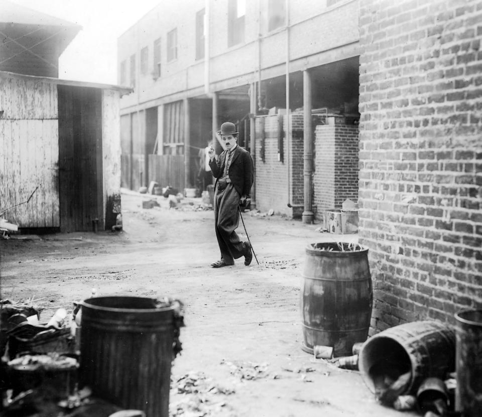 Charlie Chaplin poses in an alleyway, leaning on a cane