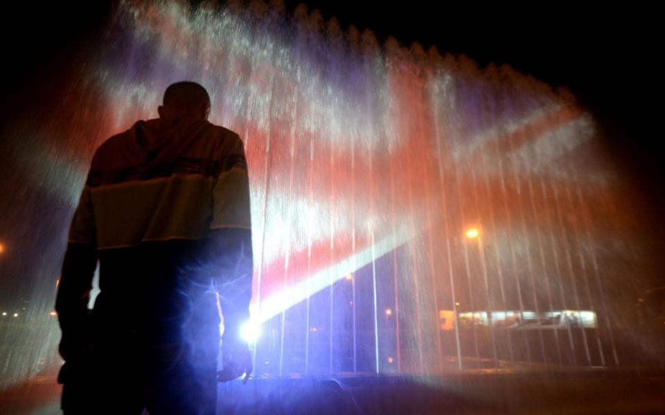 A man stands in front of a fountain illuminated with the colours of the United Kingdom flag on May 23, 2017, in Zagreb, during a tribute to victims of an attacks claimed by Islamic State which killed at least 22 people and left more than 60 injured in Manchester the day before - Credit: AFP