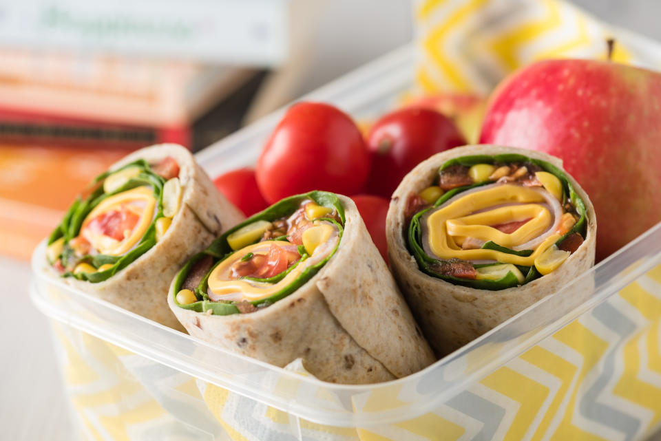 Ham and cheese wraps in lunch box with apple and tomatoes