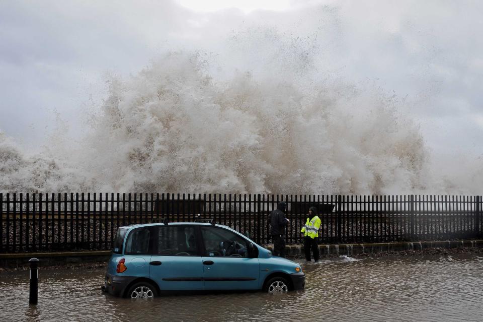 A huge wave breaks behind a car, which sits in seawater on a flooded street by the sea wall railway, in Dawlish, England, Wednesday, Feb. 5, 2014. where high tides and strong winds have created havoc in the Devonshire town disrupting road and rail networks and damaging property. (AP Photo/PA, Ben Birchall) UNITED KINGDOM OUT