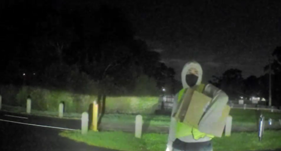 A hooded man is seeing in a fluro vest carrying boxes containing Apple Macbooks, after an abduction in Melbourne. 