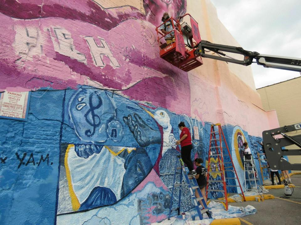 In this Thursday, May 30, 2019 photo, Brandon "BMike" Odoms, in man-lift, and students in the Young Artist Movement work on a mural in downtown New Orleans. The mural is one of five created as part of an Arts Council of New Orleans project called "Unframed." The council's executive director, Heidi Schmalbach, says the group wants New Orleans to be known for its contemporary art as much as for its music, food and culture. (AP Photo/Janet McConnaughey)