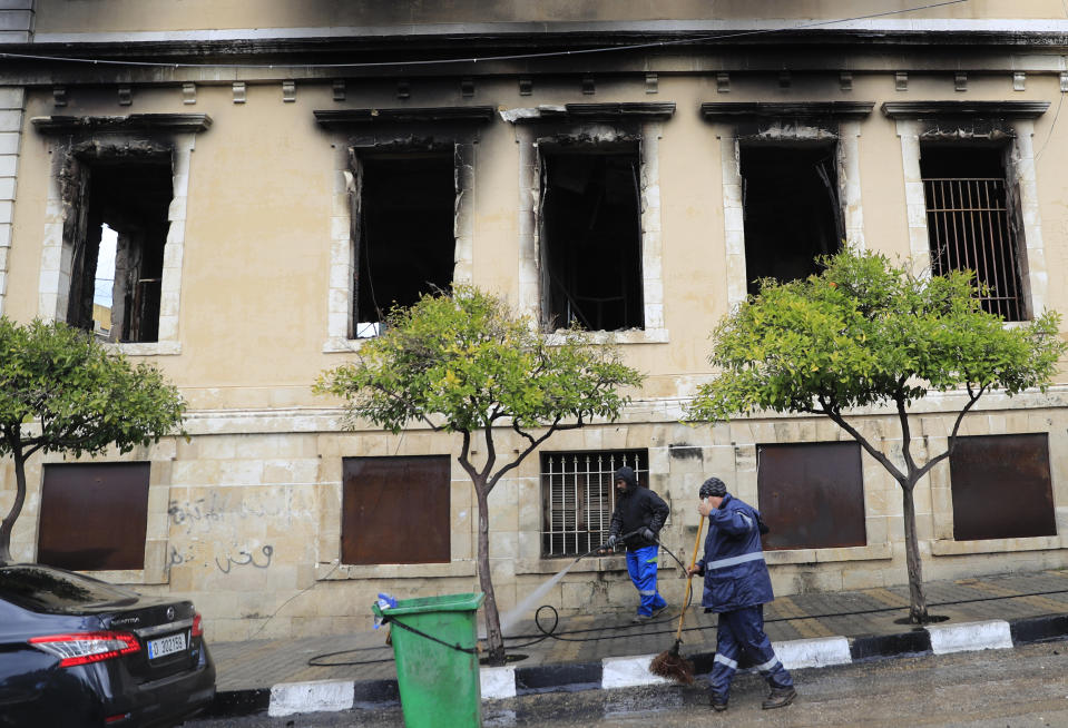 Workers clean outside the building of Tripoli municipality that was set on fire by protesters Thursday night, during a protest against deteriorating living conditions and strict coronavirus lockdown measures, in Tripoli, Lebanon, Friday, Jan. 29, 2021. (AP Photo/Hussein Malla)