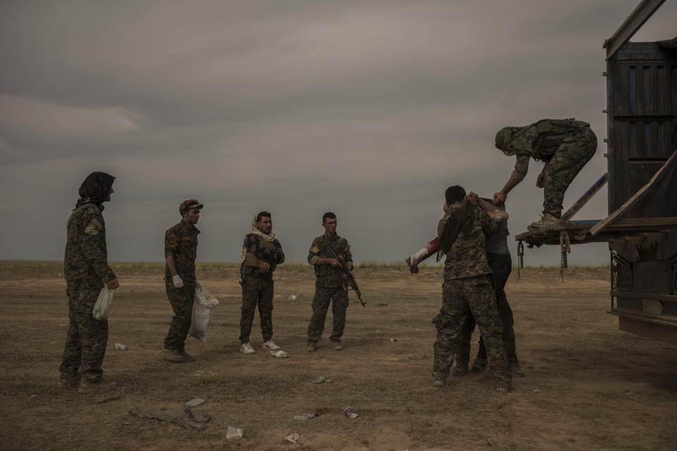 In this Sunday, March 10, 2019 photo, U.S.-backed Syrian forces stand guard as a civilian wounded by airstrikes, during an offensive on the last area held by Islamic State group extremists, arrive by truck at a reception area for evacuees, in Syria's eastern Deir el-Zour province near the Iraqi border, outside of Baghouz, Syria.