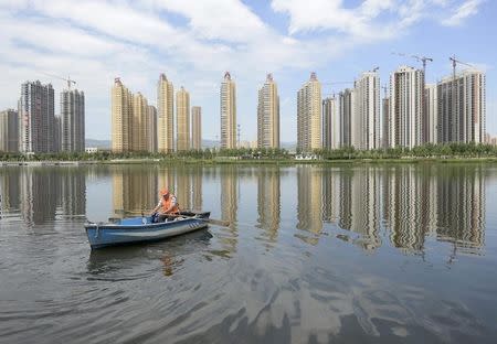 A man rows a boat on a river in front of new properties in Taiyuan, Shanxi province, July 24, 2014. REUTERS/Stringer