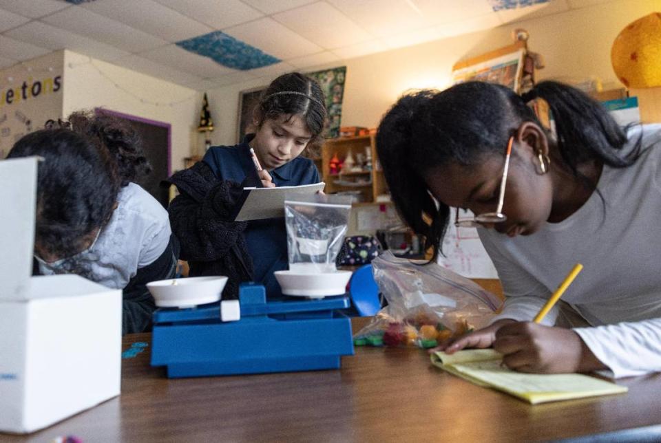 Brianna Funez, 11, from left, Evelyn Mendoza, 11, and Kyra Baker, 10, write down weights while using a scale during science tutoring at Joseph W. Grier Academy in Charlotte, N.C., on Thursday, March 9, 2023.