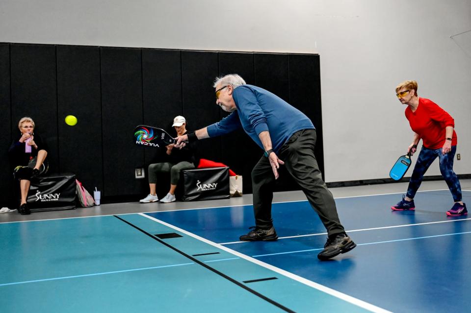 Mike Shore, left, returns the ball during a pickleball game with partner Norma Koob, right, on Friday, Jan. 27, 2023, at Court One Athletic Clubs in Lansing.