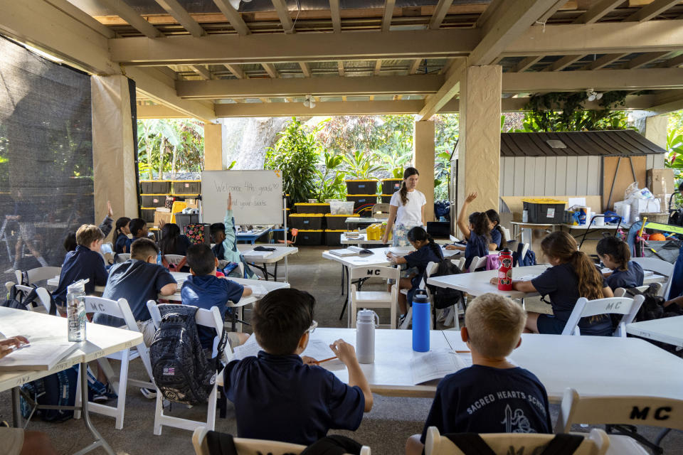 Sacred Hearts School second grade teacher Courtney Copriviza interacts with the fourth graders at their temporary school site at Sacred Hearts Mission Church on Tuesday, Oct. 3, 2023, in Lahaina, Hawaii. Sacred Hearts and other private schools across the state took in displaced public school students and offered a year of free tuition. The three public schools that survived the deadly August wildfire are set to reopen this week. (AP Photo/Mengshin Lin)