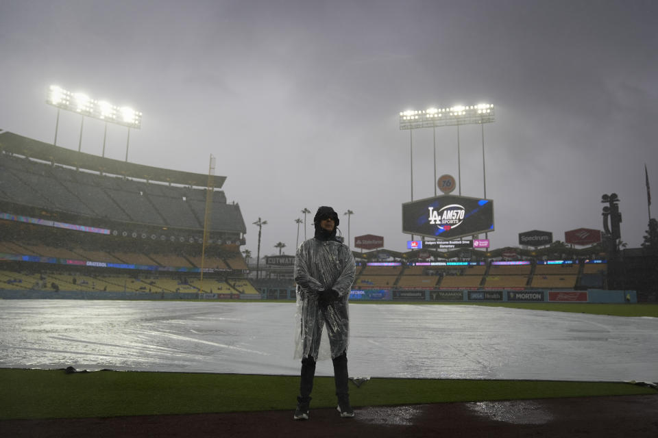 A security guard stands on the field in the rain before of a baseball game between the Los Angeles Dodgers and the San Diego Padres, Saturday, April 13, 2024, in Los Angeles. (AP Photo/Marcio Jose Sanchez)