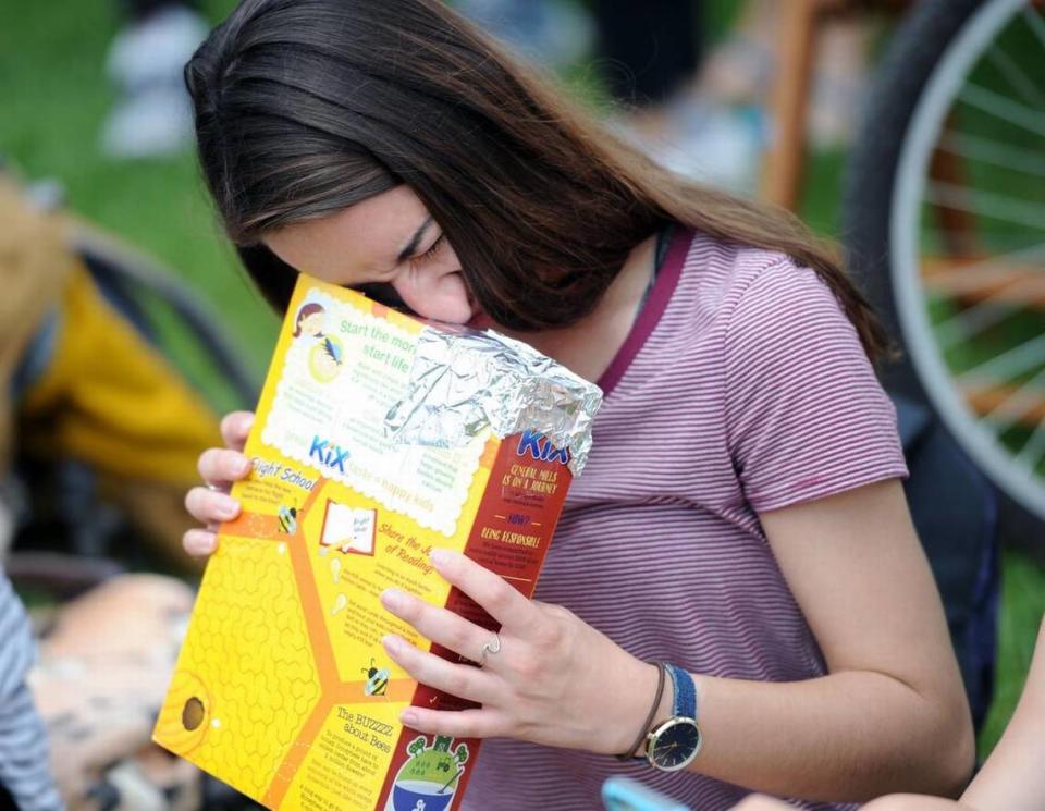 Shannon Campbell looks at the eclipse through a cereal box Monday, Aug. 21, 2017 at The Arboretum at Penn State.