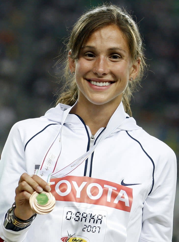 Kara Goucher smiles and poses with a bronze medal