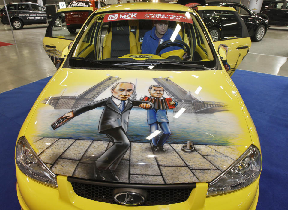 In this Friday, Oct. 21, 2011 file photo man sits in a Russian made Lada Kalina sports car with a depiction of Russian Prime Minister Vladimir Putin, left, and Russian President Dmitry Medvedev painted on the bonnet, at a car tuning company's stand during an automotive exhibition in St. Petersburg, Russia. Car makers Renault-Nissan on Thursday, May 3, 2012, signed a deal with a Russian state-owned corporation that delayed their move to acquire a controlling stake in Russian car producer Avtovaz to 2014.(AP Photo/Dmitry Lovetsky, file)