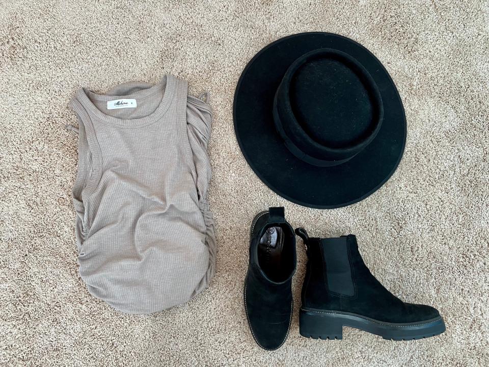 Grey dress, wide-brimmed black hat, and black booties spread on the floor.