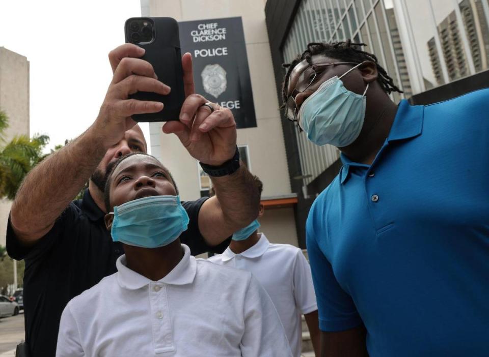 Social media coordinator for the Miami Police Department, Officer Nick Perez, left, shows Tyquane Hankerson, 14, how to set up the TikTok recording before he and fellow officers make a TikTok video outside the City of Miami Police headquarters.