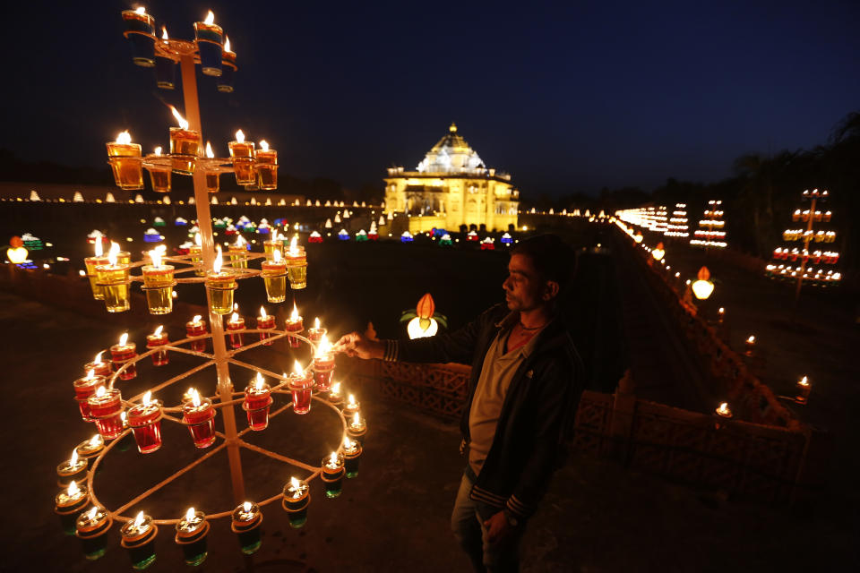 Un hombre indio enciende lámparas en el templo Akshardham al alba de Diwali, el festival de las luces en Gandhinagar, India, el martes 6 de noviembre de 2018. (AP Foto/Ajit Solanki)