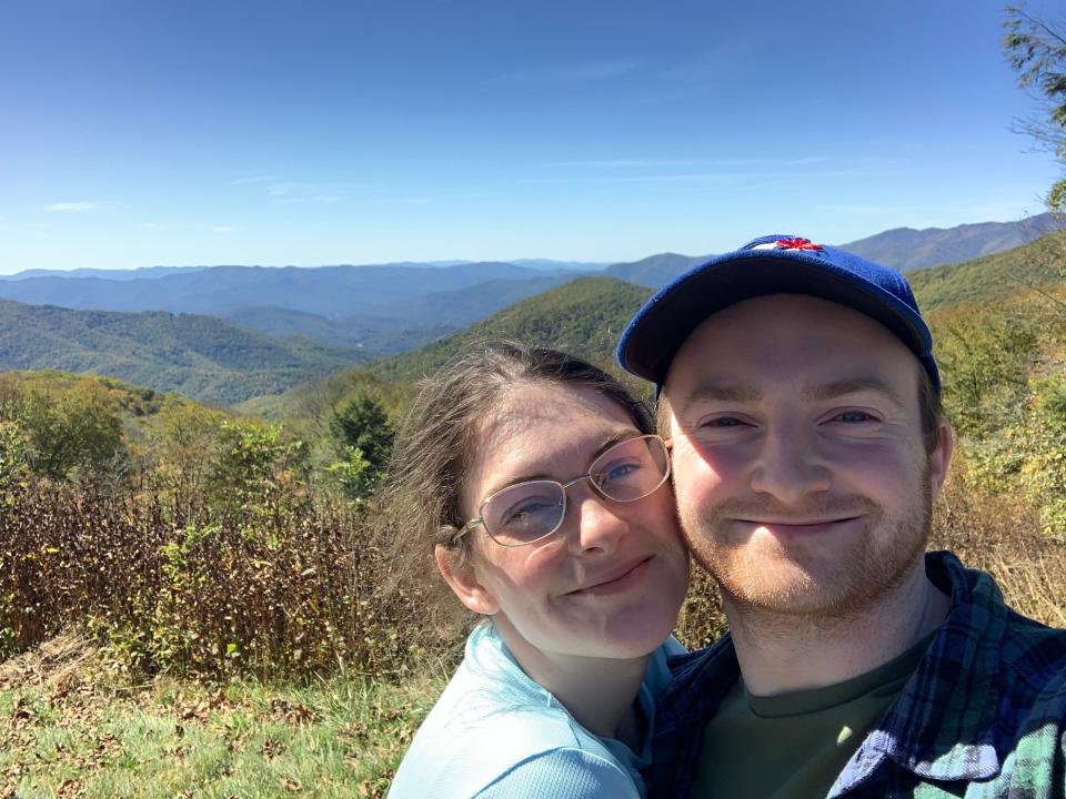 Kelsey and Ken stand in front of blue-looking mountains on their way out of Great Smoky Mountain National Park