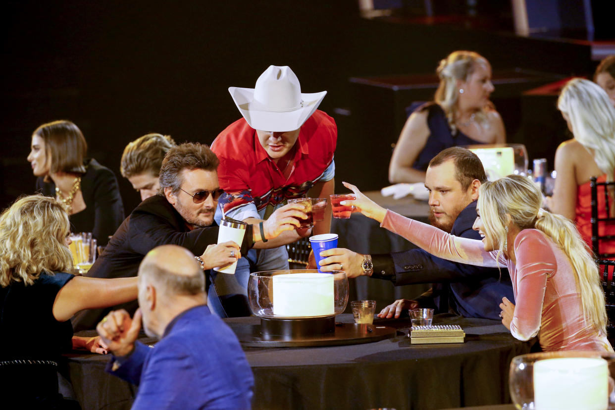 Katherine Blasingame, Eric Church, Jon Pardi, Luke Combs, and Nicole Hocking sit around a table and lean in to toast one another, not wearing face masks.