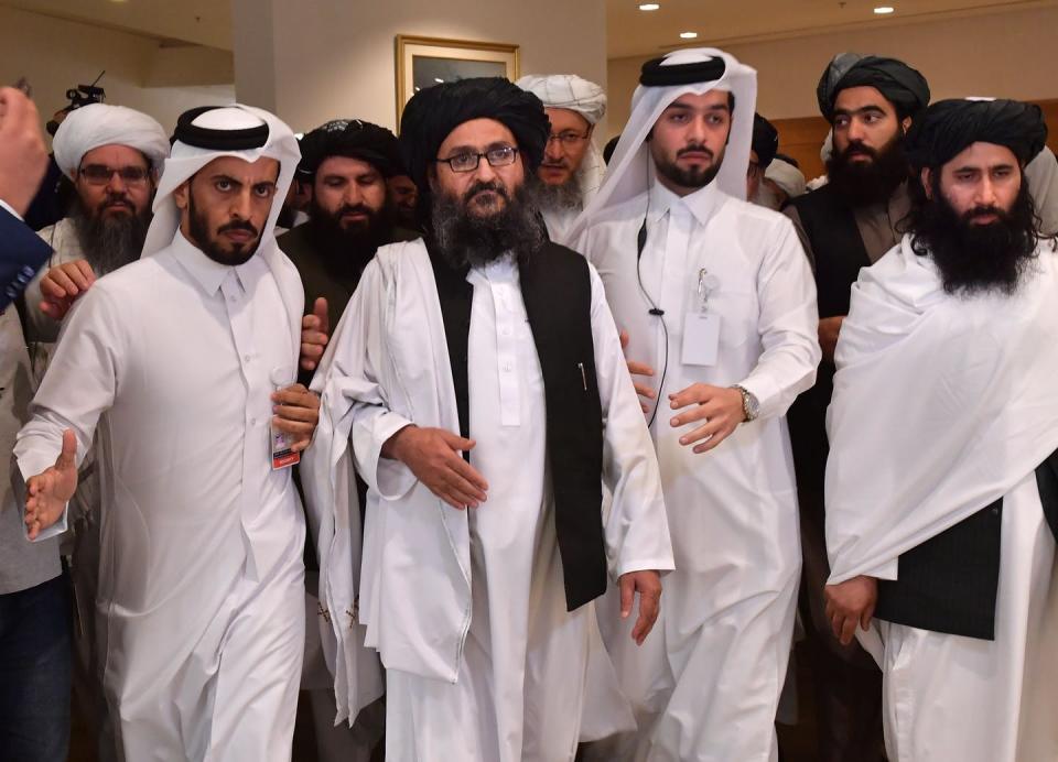 Bearded men in white robes and head coverings walk closely together in a hotel-like setting