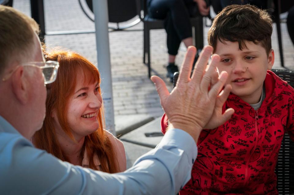 Dr. David Brown, a plastic surgeon from the University of Michigan, left, gets a high five as he helps to screen Matievi Lepinin, 10, who is joined by his mother Yana Lepinina, 33, (imiddle) of the Mykolaiv Region of Ukraine on their hotel patio in Leczna, Poland on Sunday, May 14, 2023. Lepinin was burned at age 2 after a kettle of hot water scalded his legs and feet. 