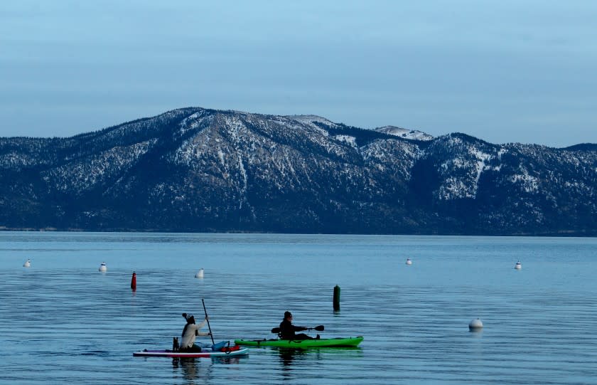 TAHOE CITY, CA. - JAN. 11, 2021. A paddle boarder and a kayaker glide across the surtface of Lake Tahoe's frigid waters on Monday, Jan. 11, 2021. Like few other places in the state, Lake Tahoe's cities and towns sit within a stew of conflicting and contradictory pandemic regulations. On the eastern shore, tourists can eat indoors, visit casinos and sleep at hotels. Nevada is open for business. But on the California side -- where three counties have overlapping jurisdiction -- commerce is shut-down -- except for the ski-slopes, which are bustling with tourists from across California and Nevada. (Luis Sinco/Los Angeles Times)