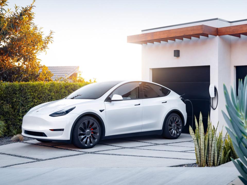 A white Tesla Model Y electric SUV charging at a home.