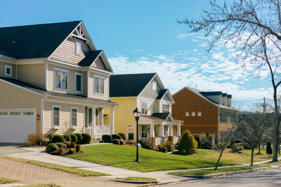 A quiet suburban neighborhood with several single-family homes, neatly manicured lawns, and clear skies