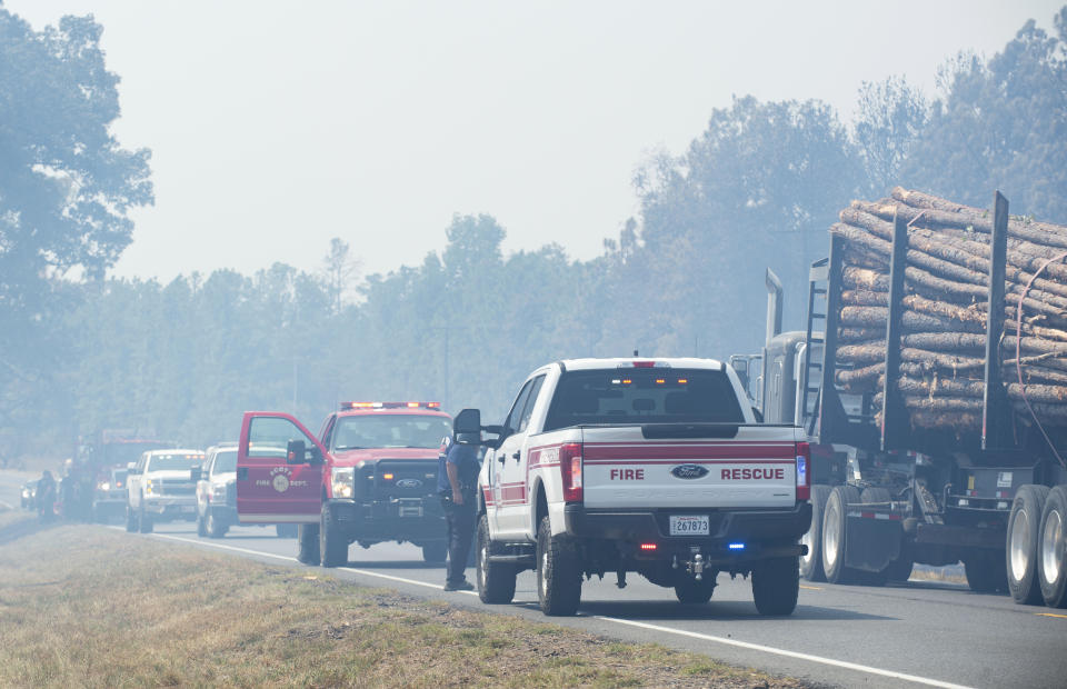 Timber trucks and fire personnel occupy Highway 27 while helping fight a wildfire, Thursday, Aug. 24, 2023, in Beauregard Parish, La. The wildfire in southwestern Louisiana forced 1,200 residents in the town of Merryville, located in Beauregard Parish, to evacuate on Thursday. (Brad Bowie/The Times-Picayune/The New Orleans Advocate via AP)