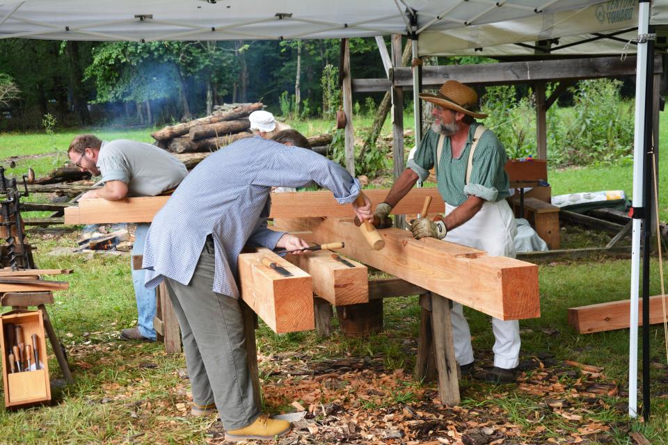 Daniel Zwick (in the background), his dad David Zwick (right), of Stoystown and Jim Wirsing (center) of Irwin, perform the log hewing demonstration. Their finished project will be the porch framing around the entrance to the Somerset Historical Center's new Pennsylvania Maple Museum when it is finished.