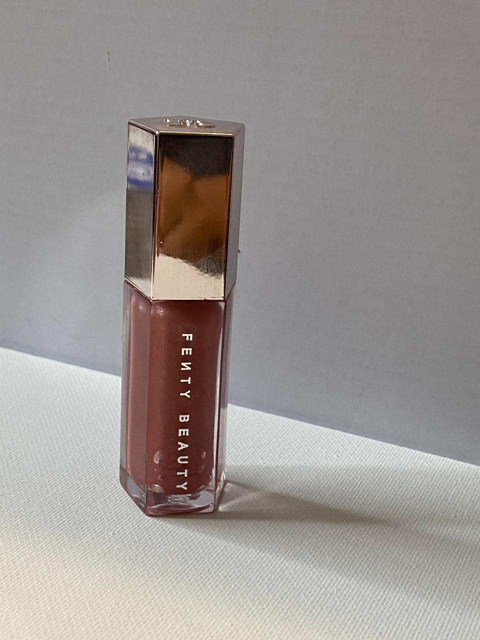 A pentagon-shaped tube of light pink lip gloss with "Fenty Beauty" on side of tube and reflective cap