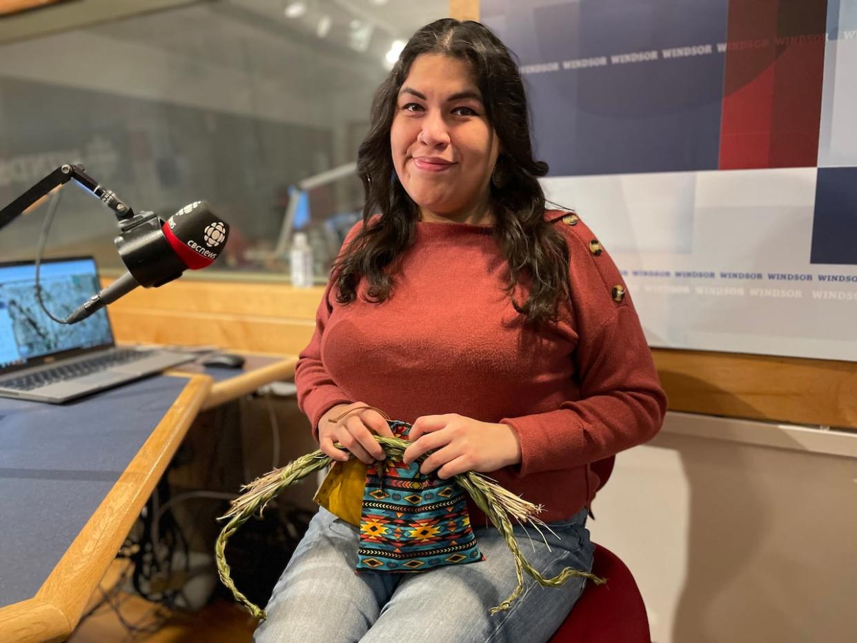 Kat Pasquach holds one of the hand-sewn pouches and braids of sweet grass — one of the ‘traditional medicines’ included in the wellness kits. (Amy Dodge/CBC - image credit)