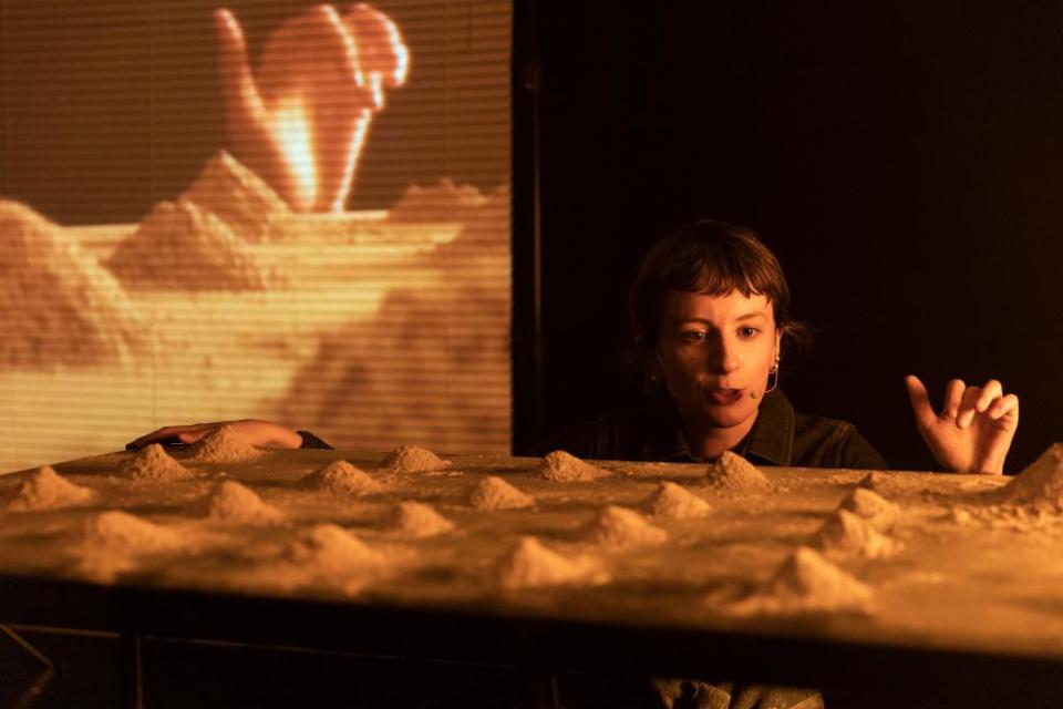 Julia Pilkington crouching  by a table on which are small heaps of sand