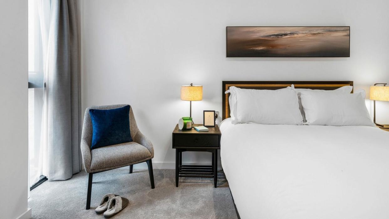 a photo of one of the apartment's interiors showing a bed and a bedside chair beside a window