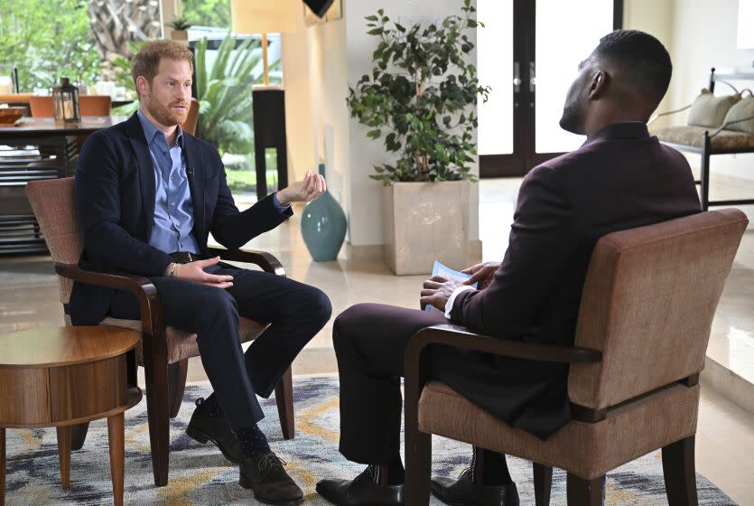 A man with red hair and a beard and a man with black hair and a beard sitting in a living room and talking to each other