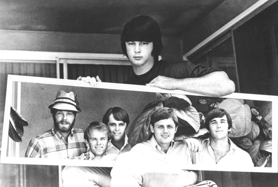 In 1967, Brian Wilson holds a mirror reflecting the band, including (L-R) Mike Love, Al Jardine, Carl Wilson, Bruce Johnston, and Dennis Wilson. (Credit: Michael Ochs Archives/Getty Images)