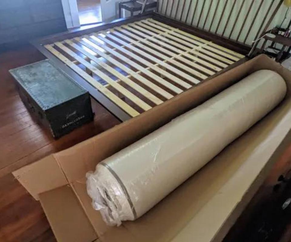 The PlushBeds Botanical Bliss Organic Latex Mattress in a box beside a bed frame.