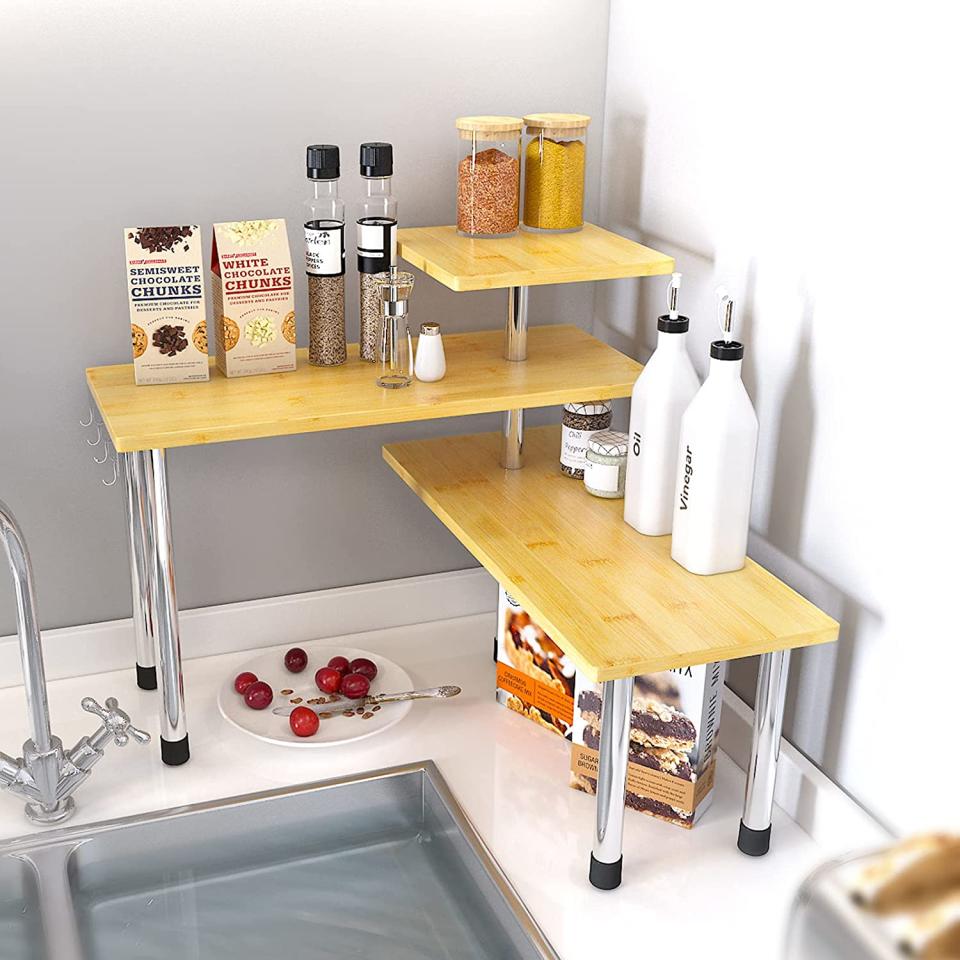 Three wooden shelves on shiny legs which form a corner unit, stacked with grocery items. SAUCE ZHAN 3 Tier Corner Shelf Bamboo Countertop Desktop Organiser, $152.90