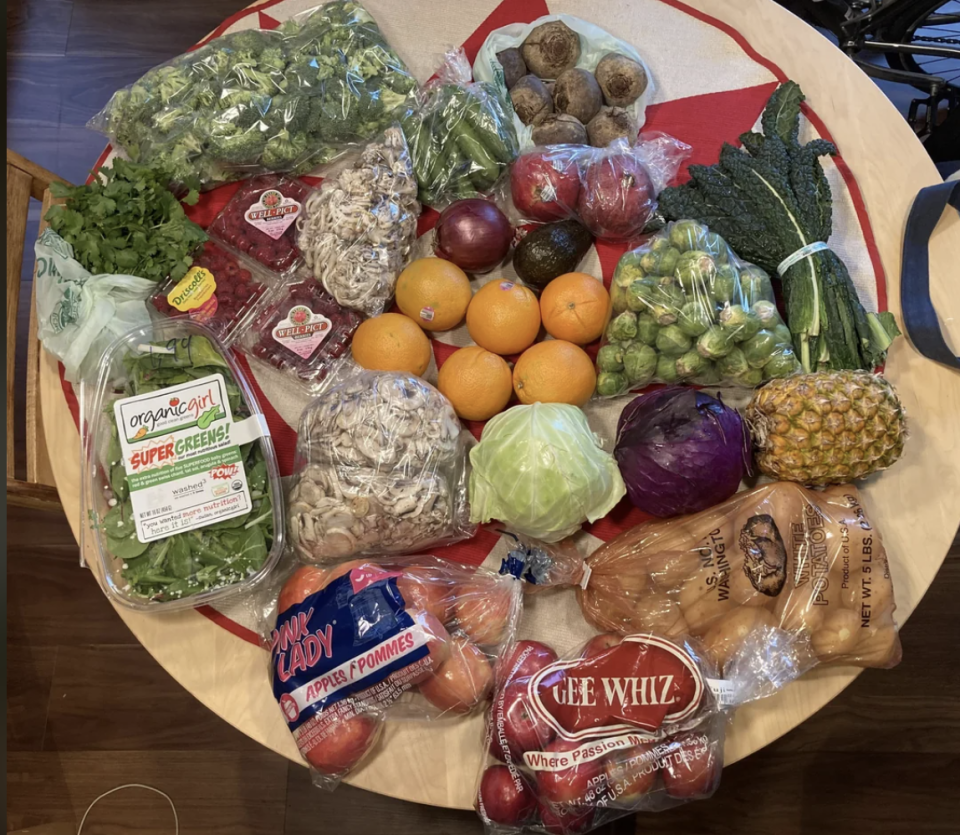 A variety of fresh vegetables and fruits on a table, including oranges, pineapple, apples, mushrooms, lettuce, kale, potatoes, and cabbage