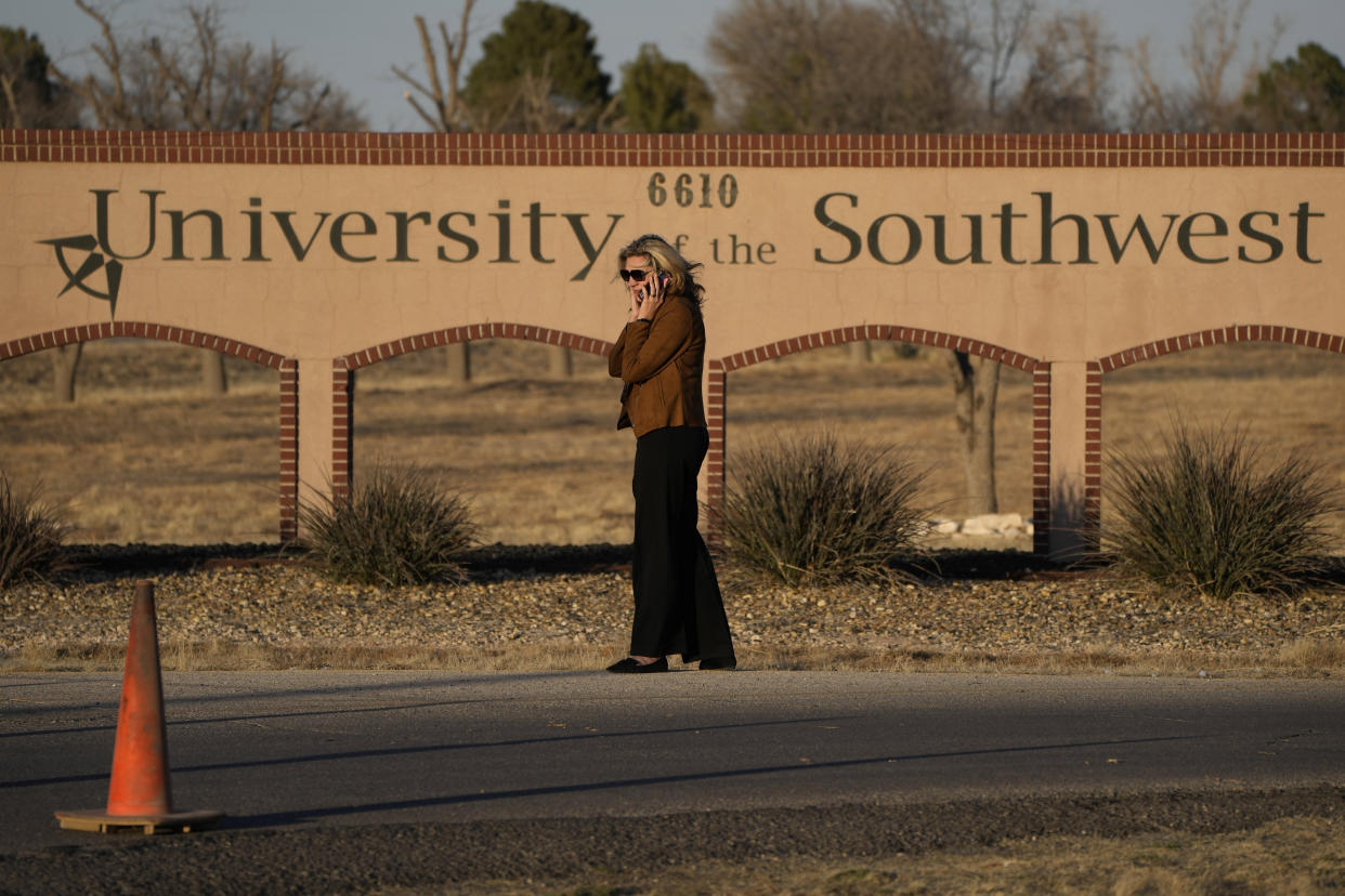 A woman stands at the entrance to the University of the Southwest, Wednesday, March 16, 2022, in Hobbs, N.M. Students and a golf coach from the school were killed in a head-on collision in West Texas on Tuesday. (AP Photo/John Locher)