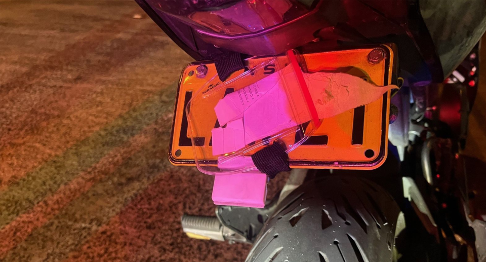 A motorbike's licence plate is obscured by a plastic sleeve containing a receipt.  