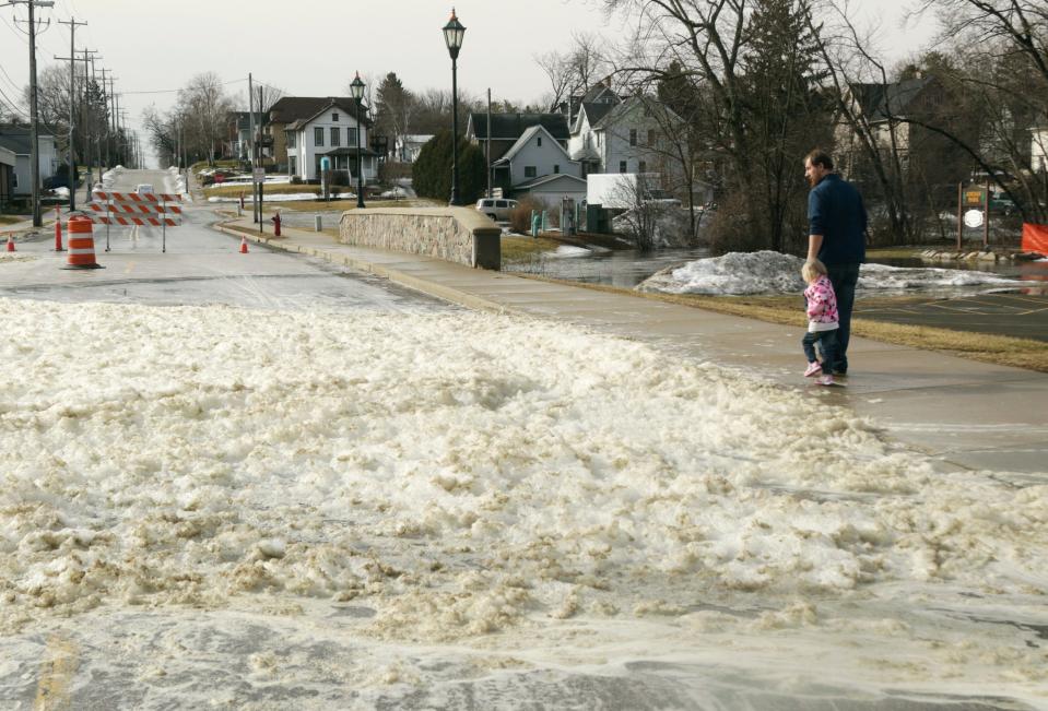 Andrew Krueger holds his daughter's hand as they walk toward a pile of foam from the Rubicon River on March 14 in Hartford, Wis. Melting snow, overnight rain and field runoff caused the large amount of foam to build up.