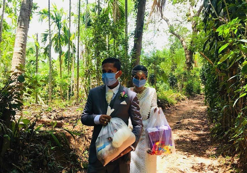 In this April 27, 2020, photo, Darshana Kumara Wijenarayana and his bride Pawani Rasanga walk with packets of food to distribute in the small town of Malimbada, about 160 kilometers (99 miles) south of the capital Colombo. The Sri Lankan couple cancelled a wedding party and instead, shared their wedding day with some of their neediest neighbors who have been economically hit due to the lock down following the new Coronavirus. (Darshana Kumara Wijenarayana via AP)